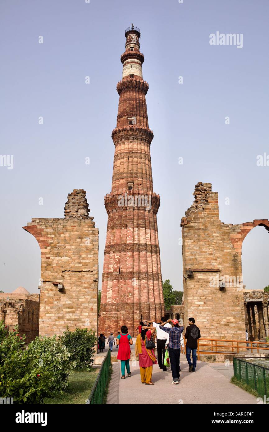 Besucher nähern sich dem Qutab Minar in Delhi, Indien, der von ruinierten Bögen der Quwwat-ul-Islam-Moschee unter einem hellen Nachmittagshimmel eingerahmt wird. Stockfoto