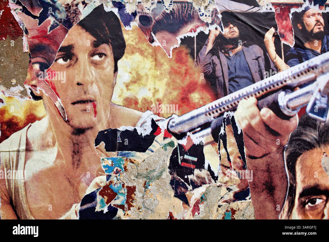 Nahaufnahme eines zerrissenen Bollywood-Actionfilmposters in Delhi, das einen blutverfluchten Protagonisten, Flammen und eine erhöhte Schrotflinte zeigt, die sich in abblätternden Papierschichten befindet. Stockfoto