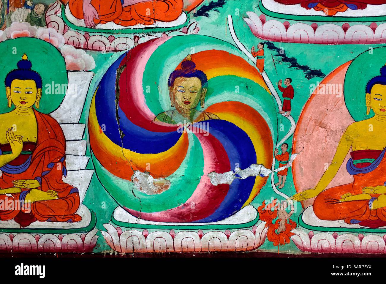 Lebendiges Wandbild im Thiksey Kloster, das ein Regenbogenmandala um einen Buddha-Kopf herum zeigt, flankiert von sitzenden Buddhas und Gläubigen in Hingabe. Stockfoto