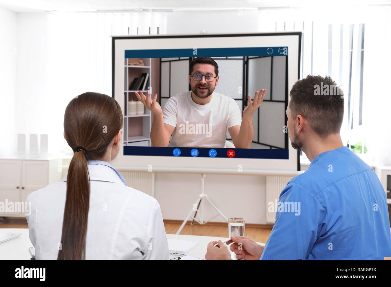 Redner, der über Online-Videochat an der Vorlesung teilnimmt. Medizinisches Personal im Konferenzraum mit Projektionsleinwand Stockfoto