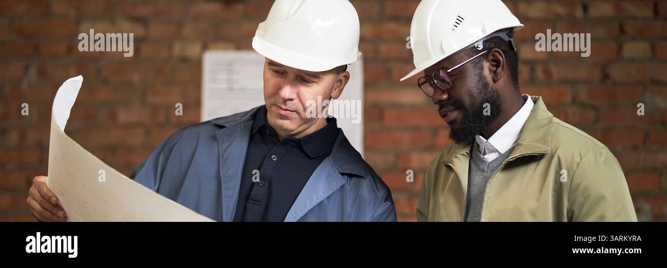 Website-Banner mit zwei hochqualifizierten birassischen Bauarbeitern, die sich den Plan ansehen Stockfoto