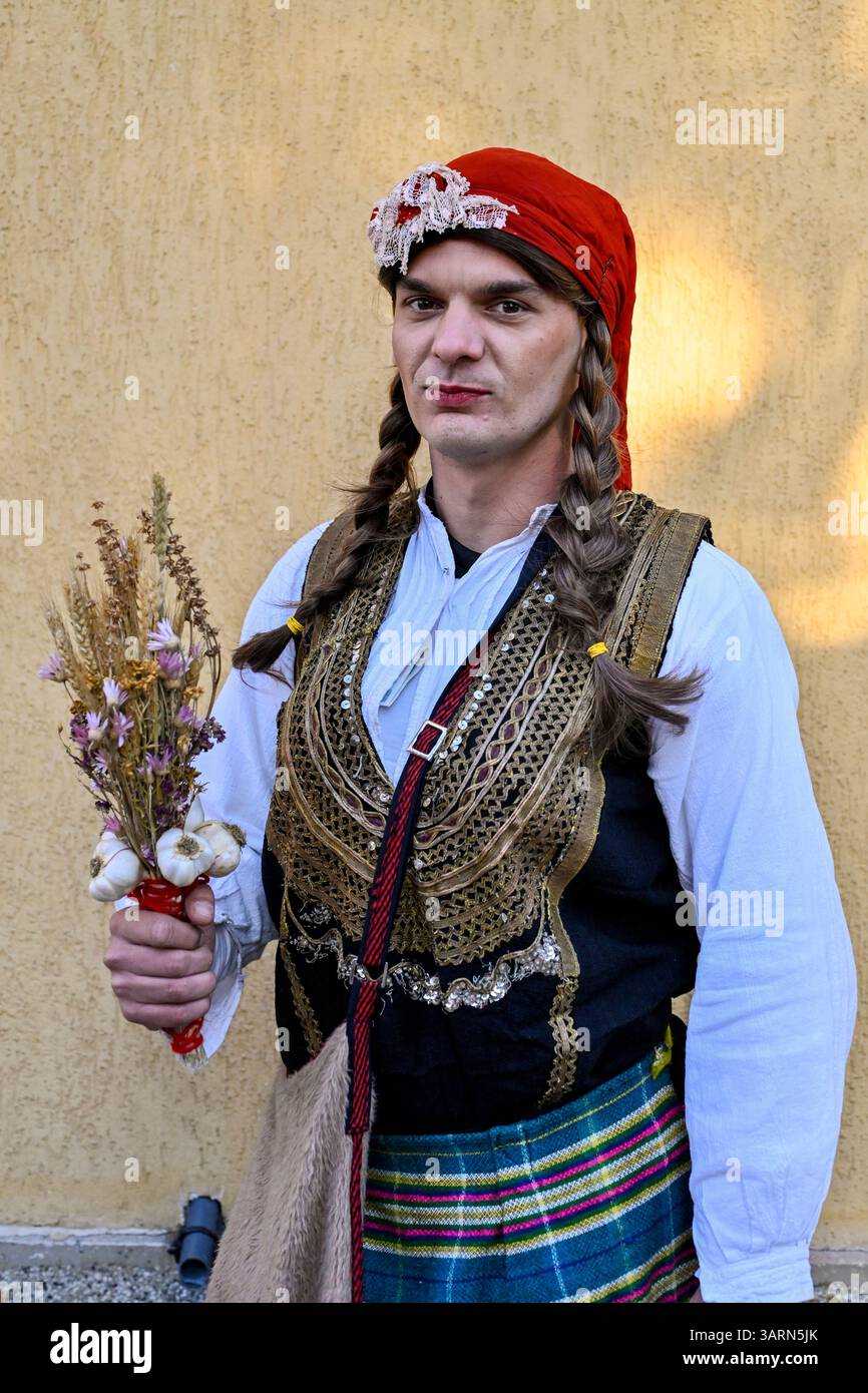 Ein Kukeri-Künstler zieht in traditioneller weiblicher Kleidung durch Breznik – ein Element ritueller Inversion, das in der Balkanmaskerade-Tradition üblich ist Stockfoto