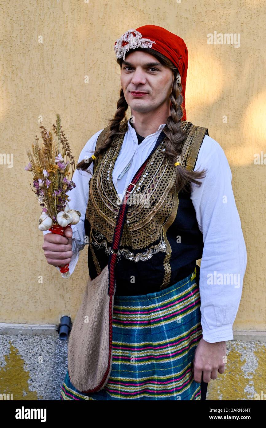 Ein Kukeri-Künstler zieht in traditioneller weiblicher Kleidung durch Breznik – ein Element ritueller Inversion, das in der Balkanmaskerade-Tradition üblich ist Stockfoto