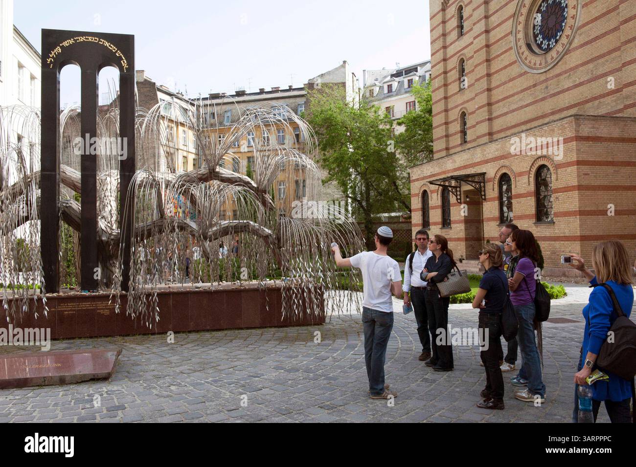 Mai 2013 - Budapest, Ungarn - Touristen mit Reiseleiter. Das Holocaust Memorial, eine Trauerweide (von Imre Varga) mit den Namen ungarischer Juden, die während des Holocaust getötet wurden, befindet sich im Raoul Wallenberg Memorial Park. Große Synagoge im jüdischen Viertel von Budapest. 1944 war die Dohany Street Synagoge Teil des jüdischen Ghettos für die Juden der Stadt und diente vielen Menschen als Zufluchtsort. Mehr als zweitausend Menschen, die im Winter 1944-1945 im Ghetto an Hunger und Kälte starben, sind im Innenhof der Synagoge begraben. Große Synagoge (Doha Stockfoto