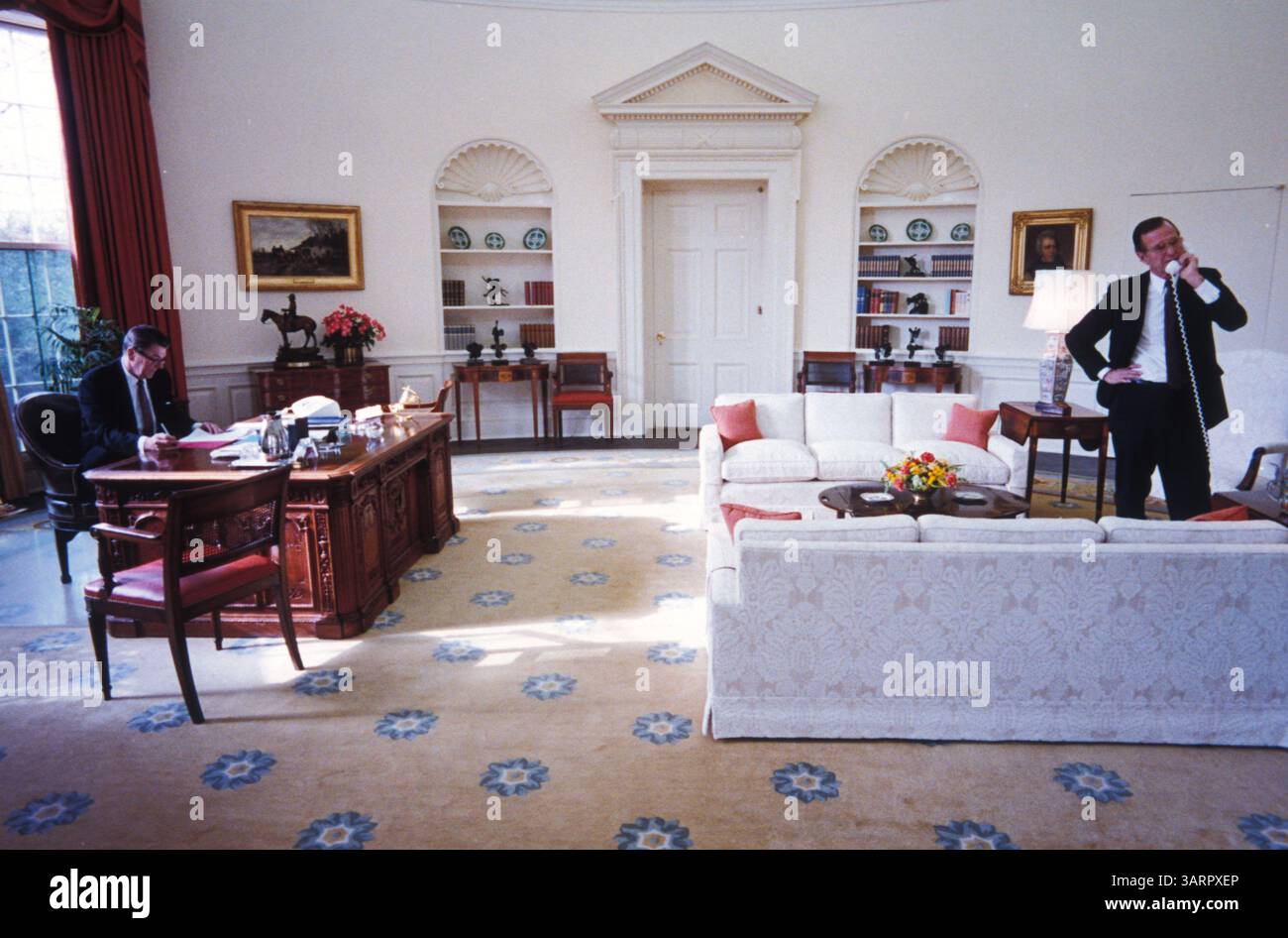 März 1982; Washington, DC, USA; der 40. US-Präsident (1981–89) RONALD WILSON REAGAN (auch bekannt als der „Great Communicator“) wurde am 6. Februar 1911 in Tampico, Illinois, geboren. Reagan leidet an der Alzheimer-Krankheit, einer degenerativen Erkrankung, die das Gehirn beeinflusst und Gedächtnisverlust und Demenz verursacht. . IM BILD: Präsident Reagan liest an seinem Schreibtisch im Weißen Haus im Oval Office, während Vizepräsident GEORGE BUSH am Telefon spricht. Jeden Donnerstag trafen sich Reagan und Bush zum Mittagessen, um politische Agenda zu besprechen. (Bild: Michael Evans/ZUMAPRESS.com) Stockfoto