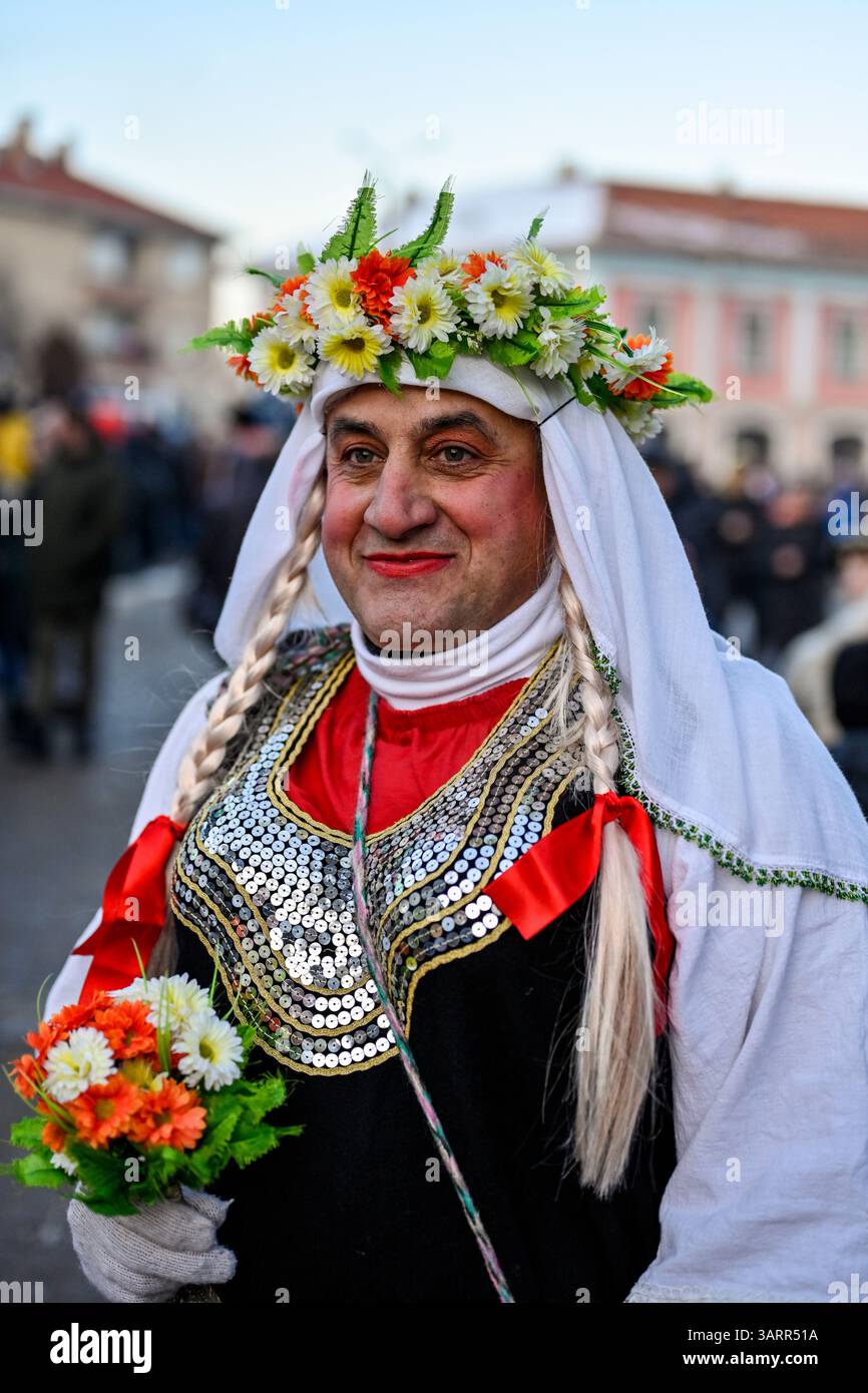 Ein Kukeri-Künstler zieht in traditioneller weiblicher Kleidung durch Breznik – ein Element ritueller Inversion, das in der Balkanmaskerade-Tradition üblich ist Stockfoto