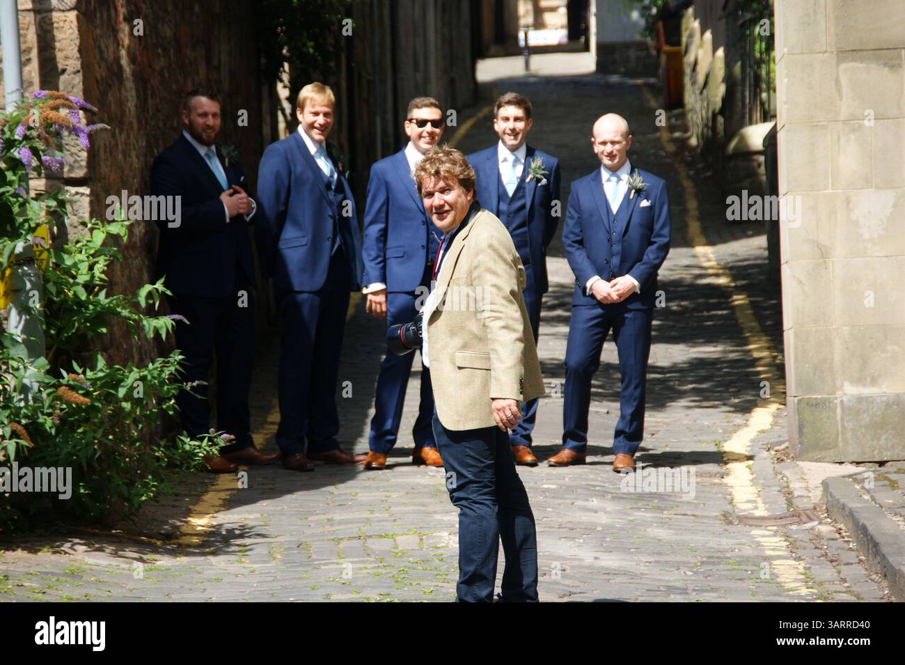 Ein Bräutigam steht mit seinen Trauzeugen, elegant gekleidet in passenden blauen Anzügen, vom Fotografen in einer malerischen Gasse in Großbritannien. Stockfoto