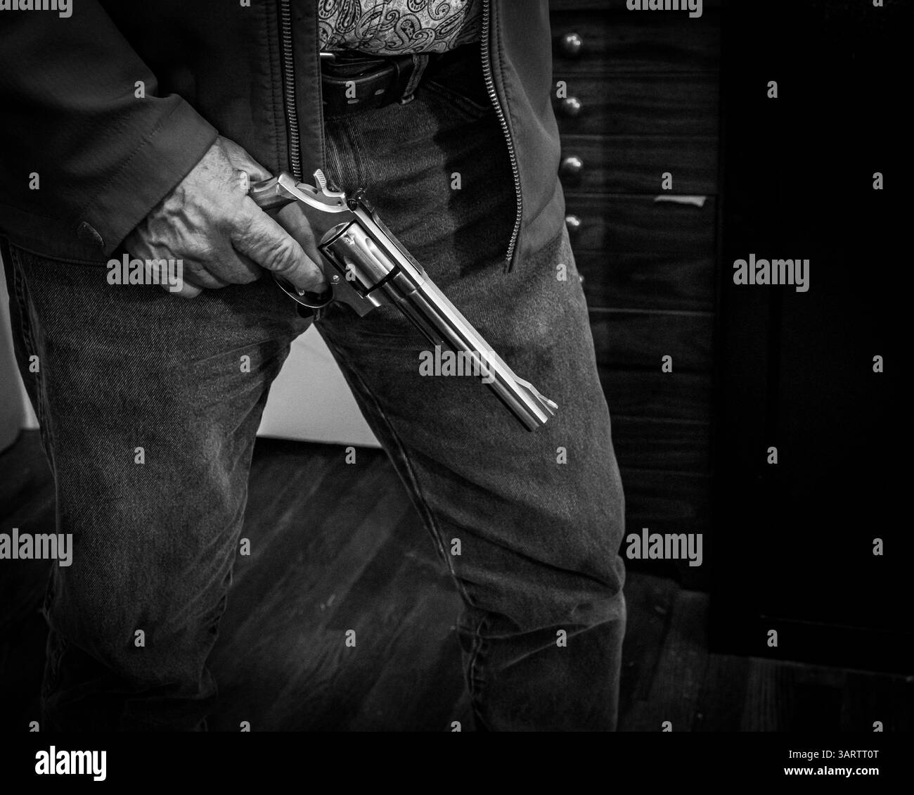 Ein Mann hält einen großen Revolver an seiner Seite. Schwarz-weiß Film Noir Stil. Stockfoto