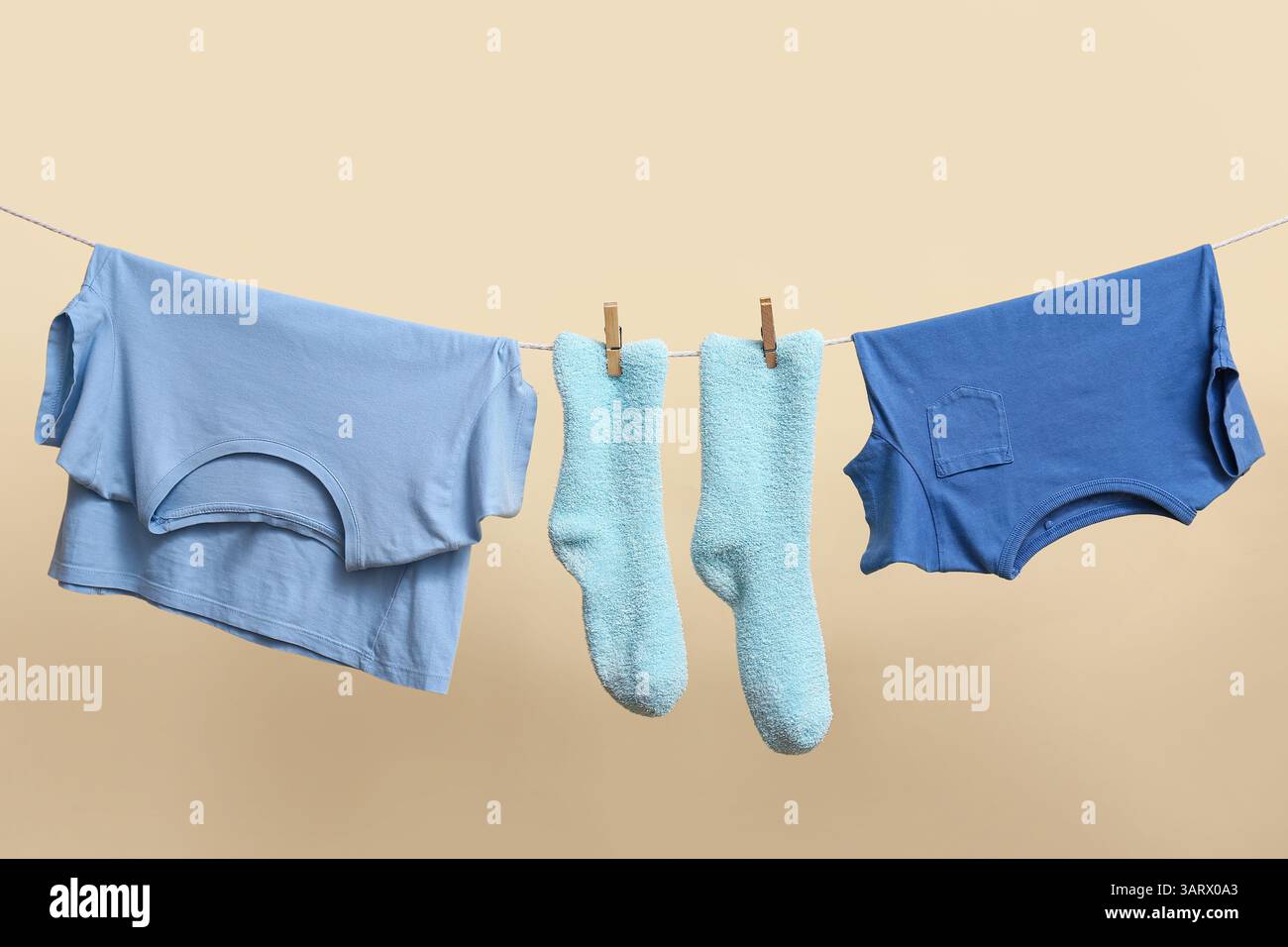 Saubere Socken und T-Shirts, die an einem Seil an der Farbwand hängen Stockfoto