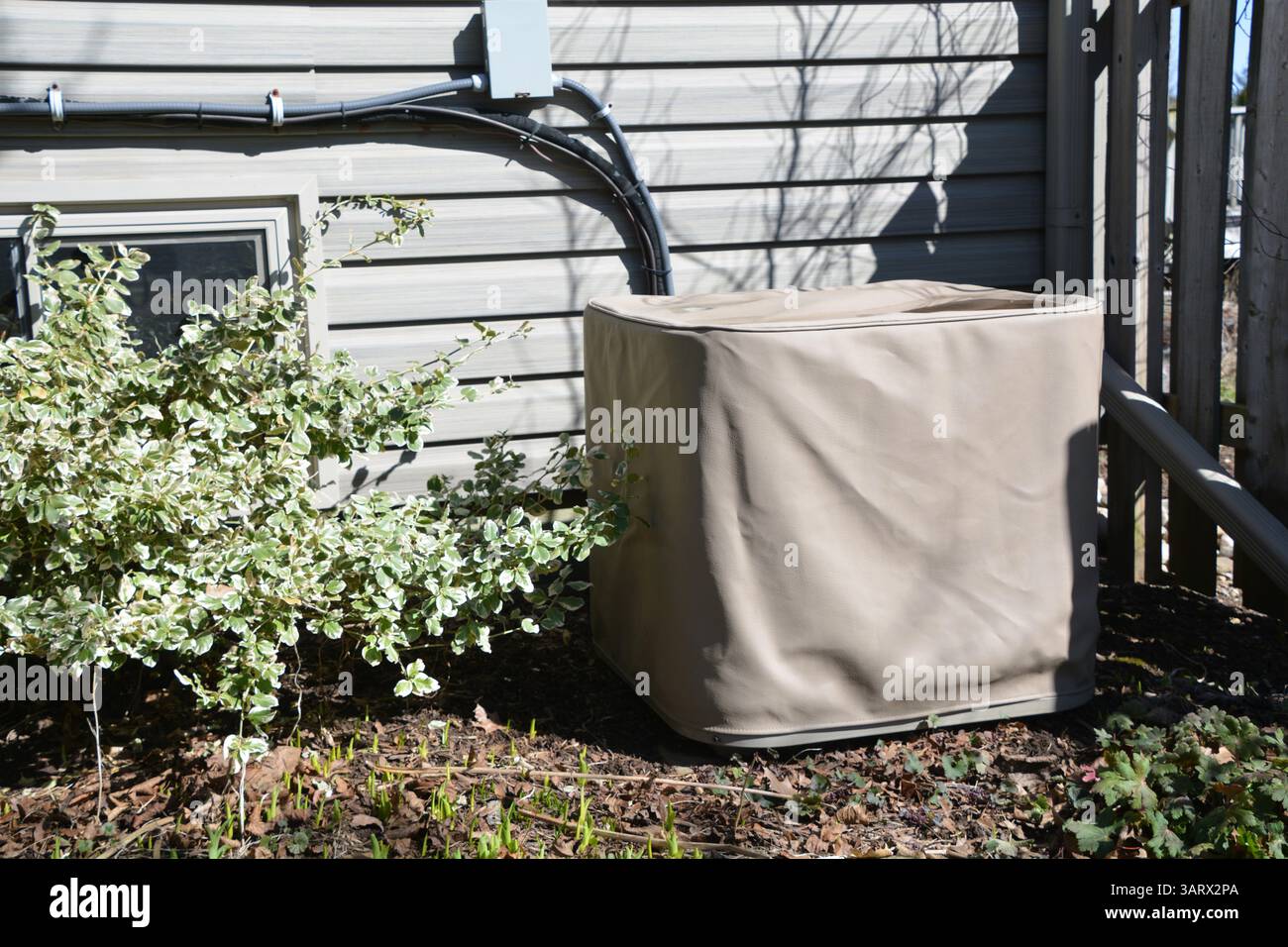 Eine zentrale Klimaanlagen-Kondensatoreinheit im Freien ist mit einer beigefarbenen Schutzabdeckung vor einem Wohnhaus abgedeckt. Stockfoto Eine zentrale Klimaanlagen-Kondensatoreinheit im Freien ist mit einer beigefarbenen Schutzabdeckung vor einem Wohnhaus abgedeckt. Stockfoto