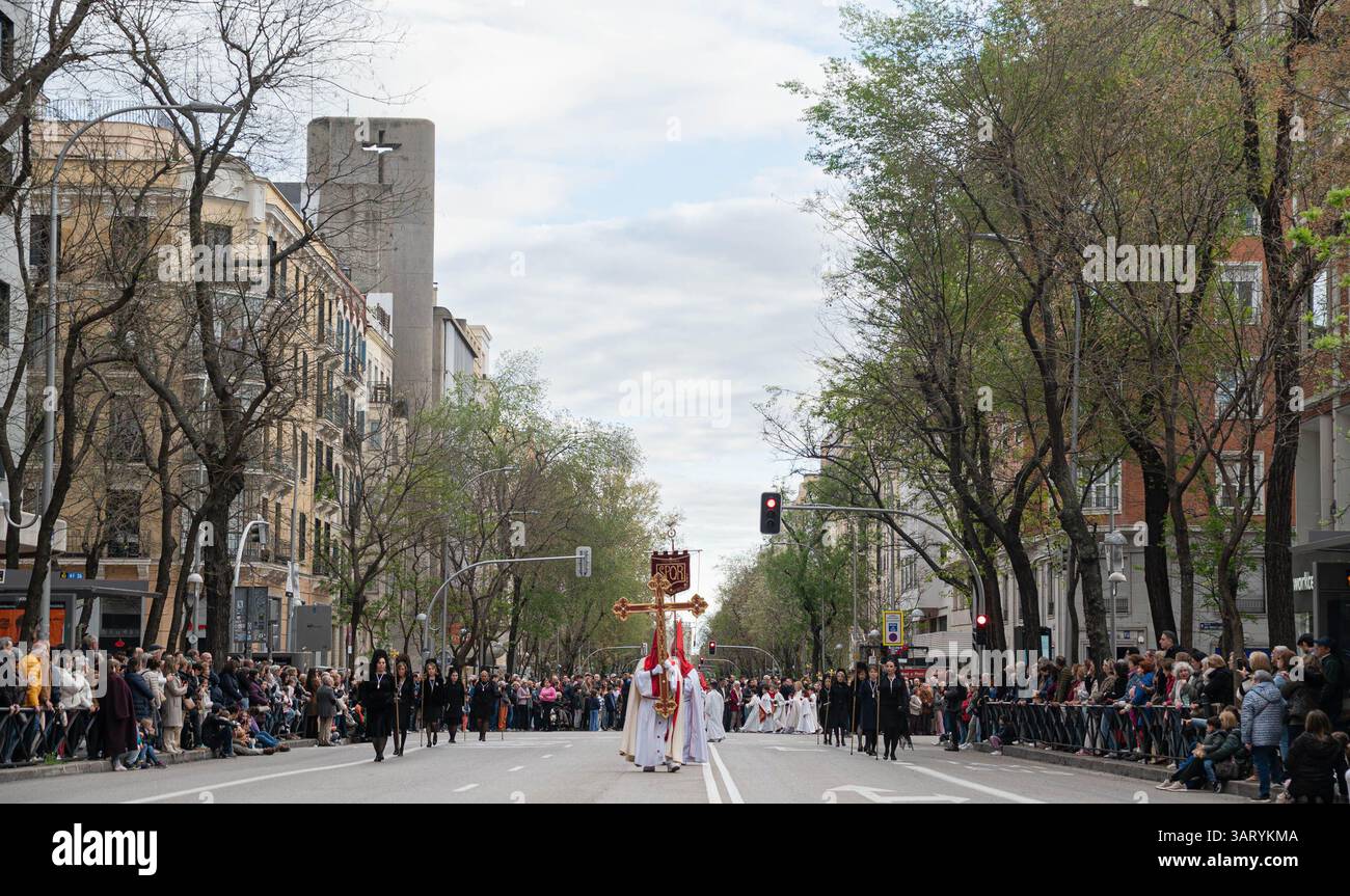 Madrid, Spanien. April 2025. Panoramablick auf eine Karwochenprozession mit Nazarenern, die ein großes, reich verziertes Kreuz durch eine breite Straße der Stadt tragen. Die Karwochenprozession in Madrid ist eine tief verwurzelte katholische Tradition, die in der Woche vor Ostern stattfindet. Mit feierlichen Paraden mit religiösen Wagen, traditioneller Musik und Teilnehmern in Bußgewändern spiegelt die Veranstaltung das reiche spirituelle Erbe Spaniens wider und zieht jedes Jahr Tausende von Zuschauern an. Quelle: SOPA Images Limited/Alamy Live News Stockfoto