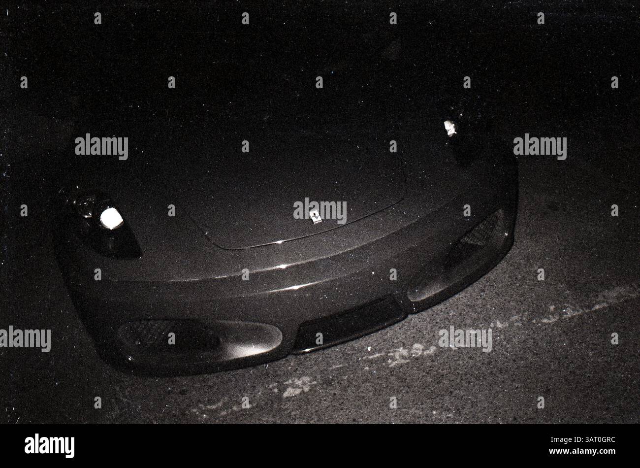 Eleganter Sportwagen, der unter dem Sternenhimmel geparkt wird und seine eleganten Kurven und seine auffällige Präsenz bei Nacht auf einer Stadtstraße offenbart: Ferrari Front Grille und Prancing Horse Emblem bei Nacht in kontrastreichem Schwarz-weiß-Film, Peking, China Stockfoto