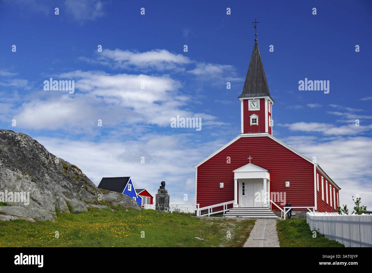 Rote Kirche mit weißem Eingang und Turm, Skulptur nebenan unter blauem Himmel, Erlöserkirche, Altstadt der Hauptstadt Grönlands, Nuuk, GRE Stockfoto