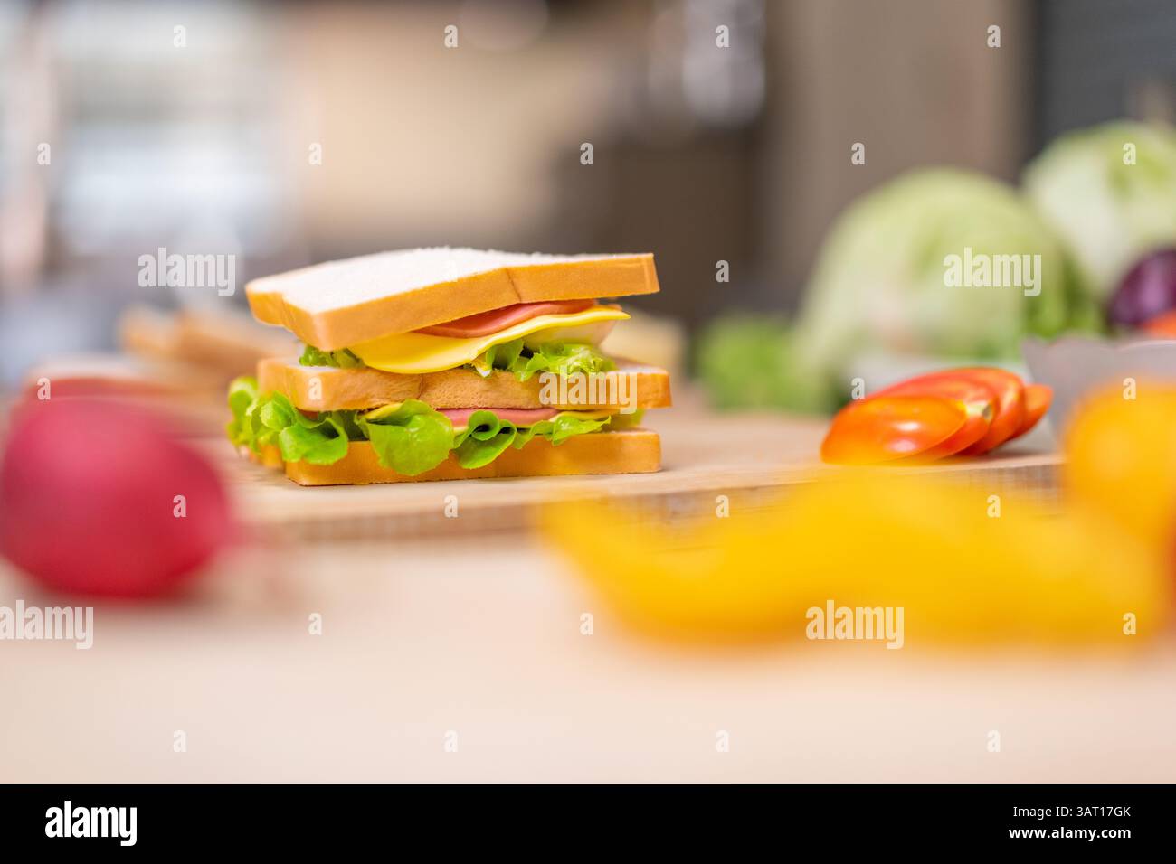 Ein köstliches hausgemachtes Sandwich mit frischem Salat, Käse, Ei und Fleisch auf einem hölzernen Schneidebrett, umgeben von farbenfrohem Gemüse. Erfasst Stockfoto