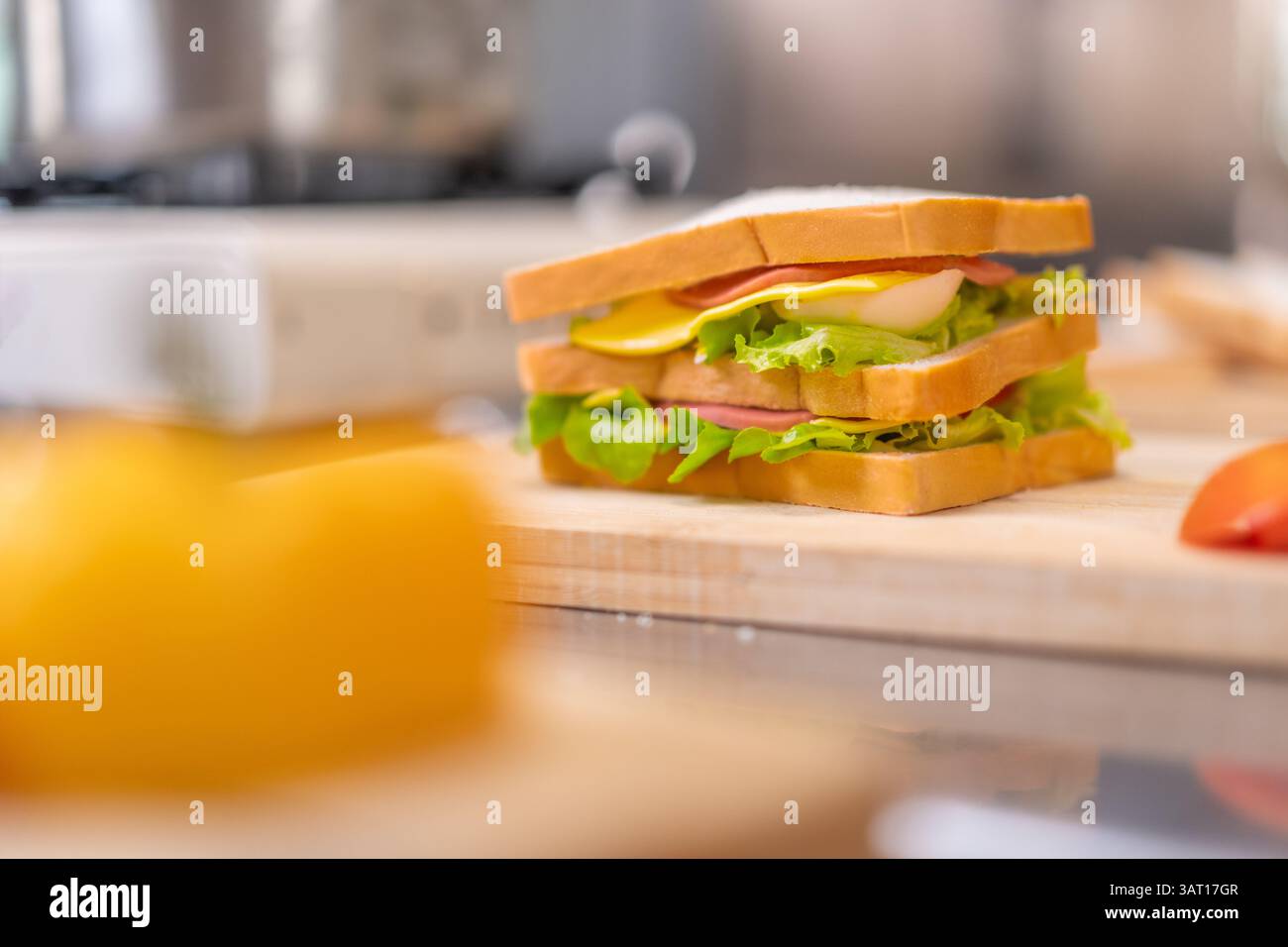 Ein köstliches hausgemachtes Sandwich mit frischem Salat, Käse, Ei und Fleisch auf einem hölzernen Schneidebrett, umgeben von farbenfrohem Gemüse. Erfasst Stockfoto