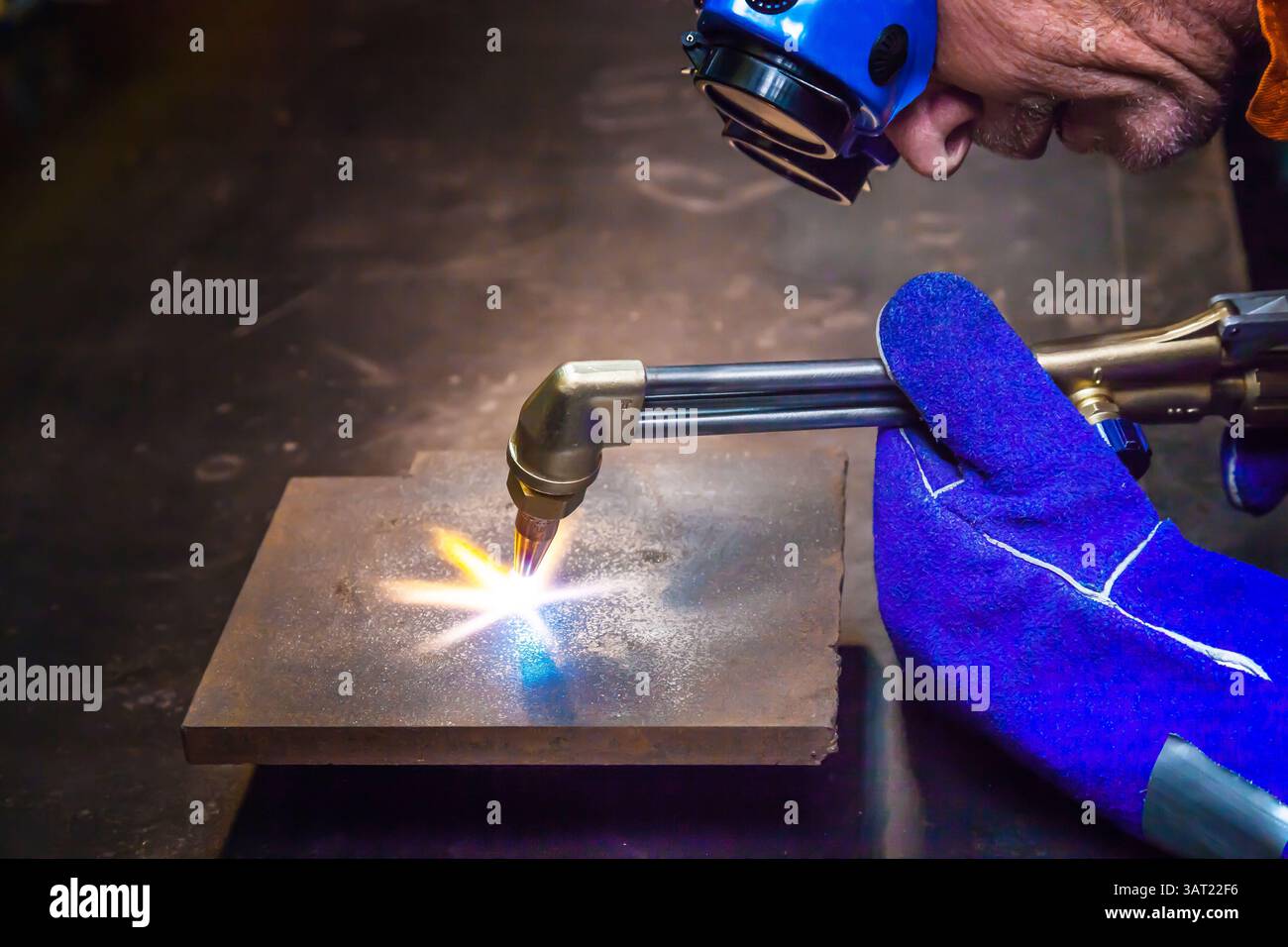 Ein Mann mit Schutzbrille und Handschuhen erhitzt ein Blech mit einem Gasschneider, um es abzuschneiden. Stockfoto