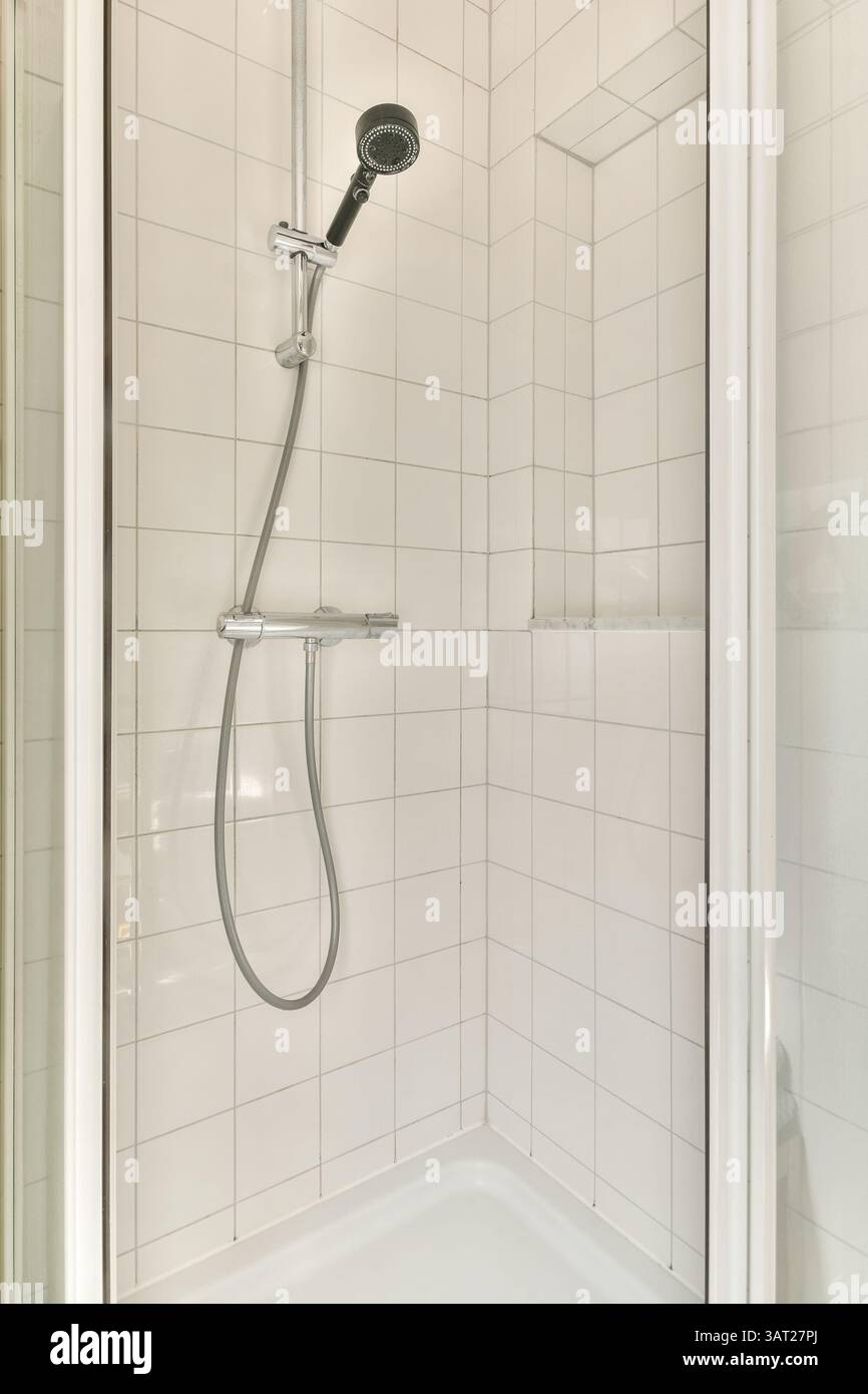 Eine elegante und minimalistische Duschkabine mit weiß gefliesten Wänden und einem modernen Handbrause, perfekt für moderne Badezimmer. Stockfoto