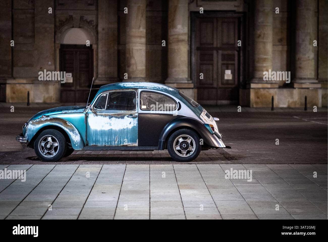 Ein Oldtimer, der nachts auf einer kopfsteingepflasterten Straße parkt und ein verwittertes blau-schwarzes Äußere zeigt. Die Szene wird durch sanfte Beleuchtung beleuchtet, hoch Stockfoto
