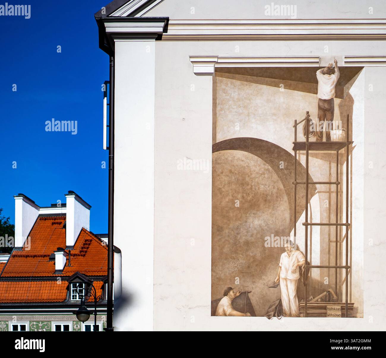 Ein Wandgemälde, das Arbeiter zeigt, die eine Wand malen und eine historische Arbeitsszene zeigen. Das Kunstwerk steht vor einem klaren blauen Himmel, mit einer Gebäudefeatur Stockfoto