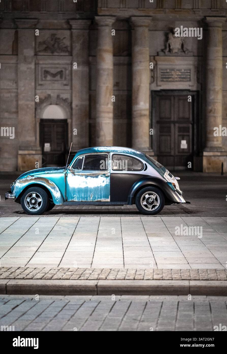 Ein Oldtimer, der nachts auf einer kopfsteingepflasterten Straße parkt und von sanften Straßenlaternen beleuchtet wird. Das Fahrzeug hat eine einzigartige zweifarbige Lackierung mit einer verwitterten Toilette Stockfoto