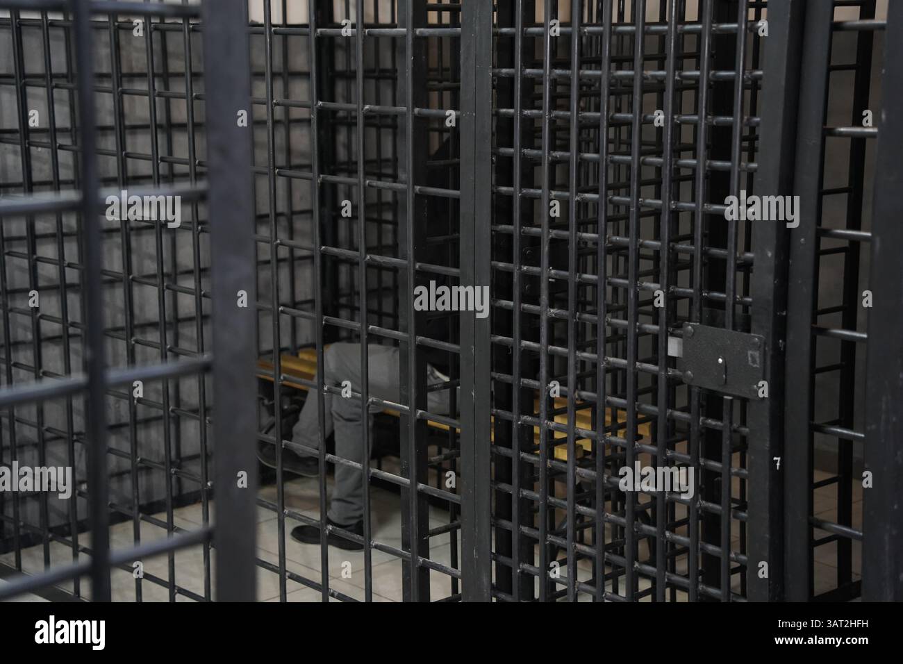 Ein Häftling mit Kapuze sitzt in einer geschlossenen, vorübergehenden Zelle. Stockfoto