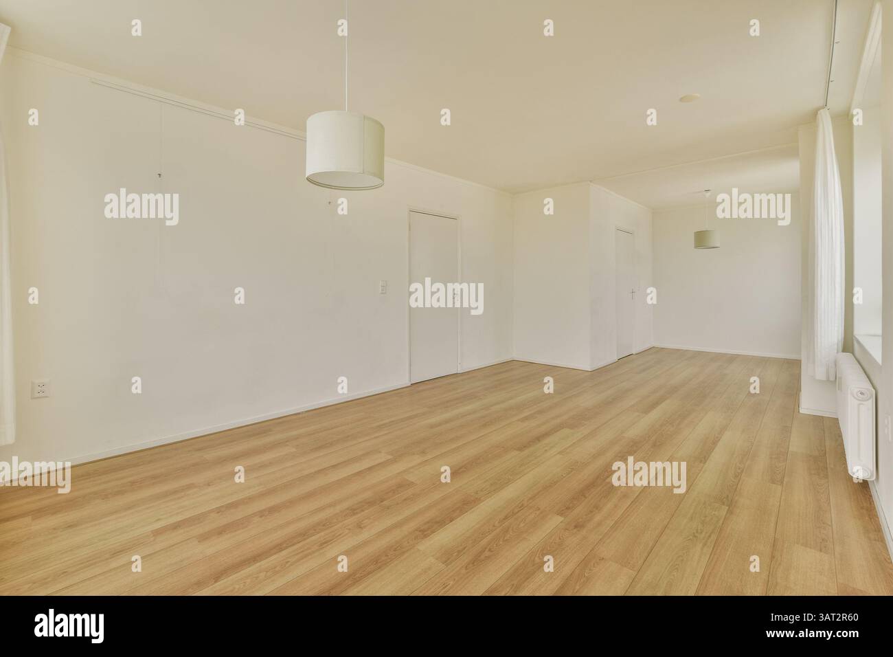 Ein geräumiges und minimalistisches Zimmer mit hellen Wänden, Holzfußboden und einer einzelnen Pendelleuchte, ideal für modernes Wohnen. Stockfoto