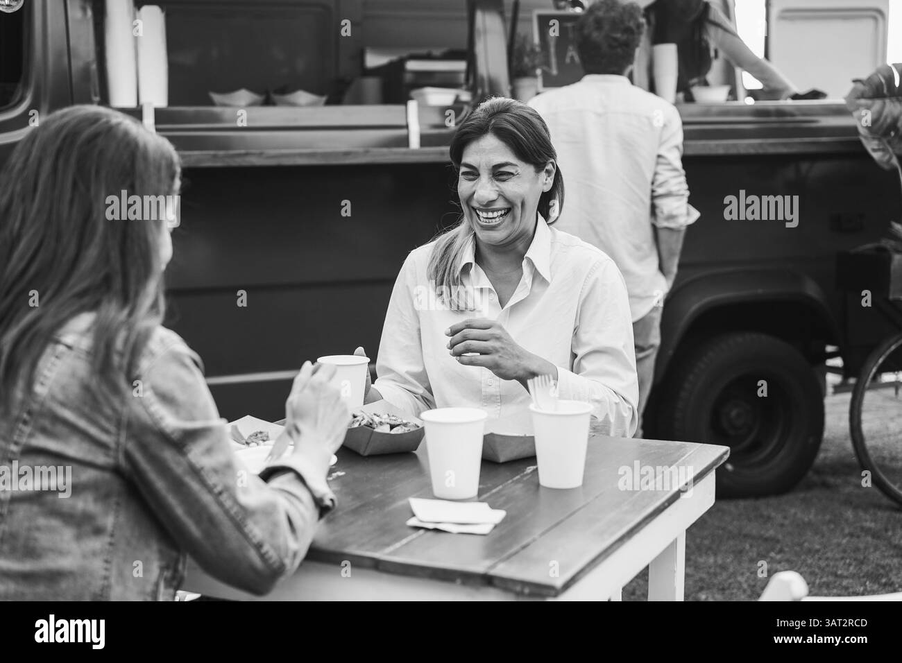 Multirassische Menschen essen zusammen vor Plastikwagen im Freien - Freundinnen, die Spaß haben, draußen zu Abend zu essen - Fokus Stockfoto