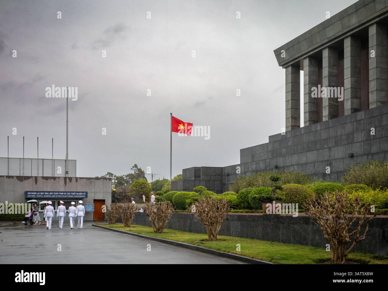 Weißuniformierte Soldaten der Ehrengarde des Ho-Chi-Minh-Mausoleum-Kommandos gehen neben dem Mausoleum und einer vietnamesischen Flagge, Hanoi, Vietnam Stockfoto