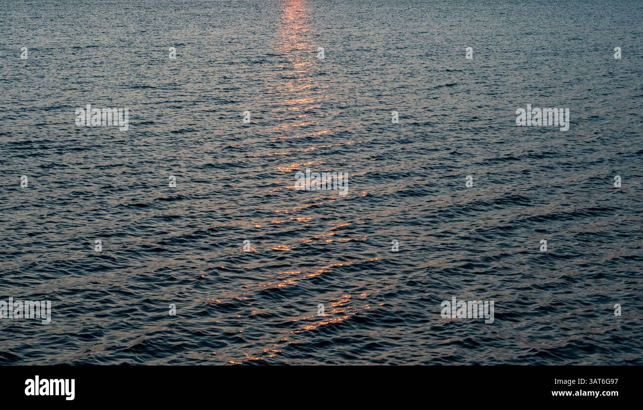 Der Sonnenaufgang spiegelte sich in den Wellen des Rappahannock River, einer weiten Wasserfläche mit sanften Wellen, die ein warmes, rötliches Licht reflektieren Stockfoto