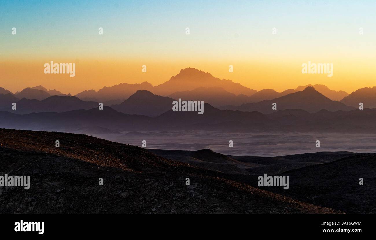Ein atemberaubender Blick auf die geschichteten Berge bei Sonnenuntergang, mit einem goldenen Himmel, der in tiefblaues Blau übergeht. Der Vordergrund weist felsiges Gelände auf, während der bac Stockfoto