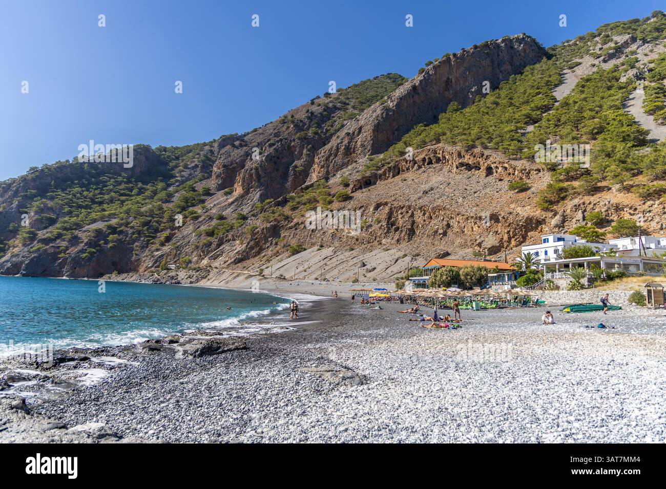 Kreta, Griechenland - 18. Oktober 2024: Strand von Agia Roumeli am Ende der Samaria-Schlucht, wo kristallblaues Meer auf dramatische Klippen und Kiefernhügel trifft Stockfoto