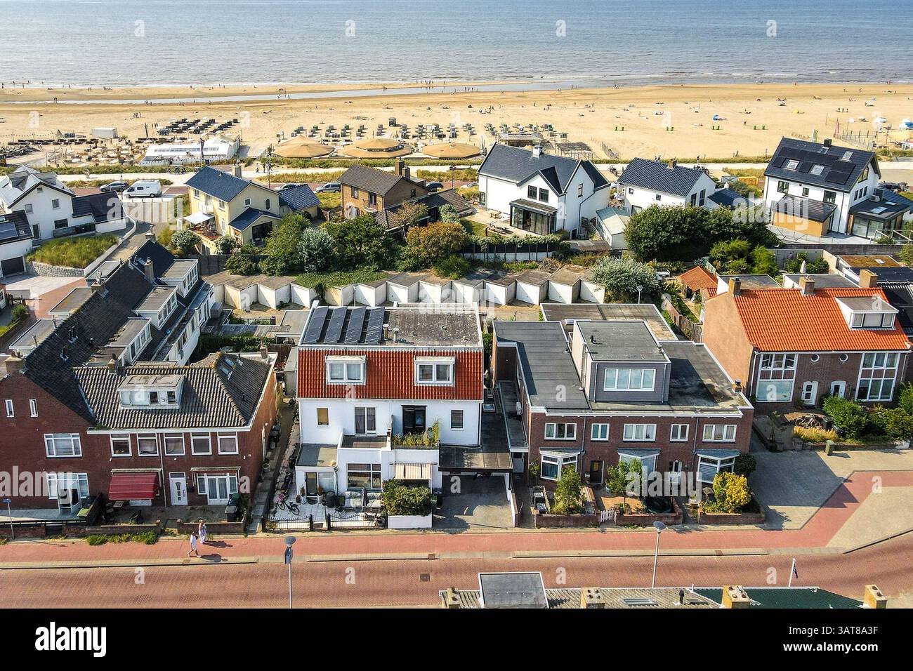 Aus der Vogelperspektive mit Häusern an einem Sandstrand, mit Sonnenschirmen und Sonnenanbetern in der Ferne. Schwerpunkt auf Architektur und Naturschönheit. Stockfoto