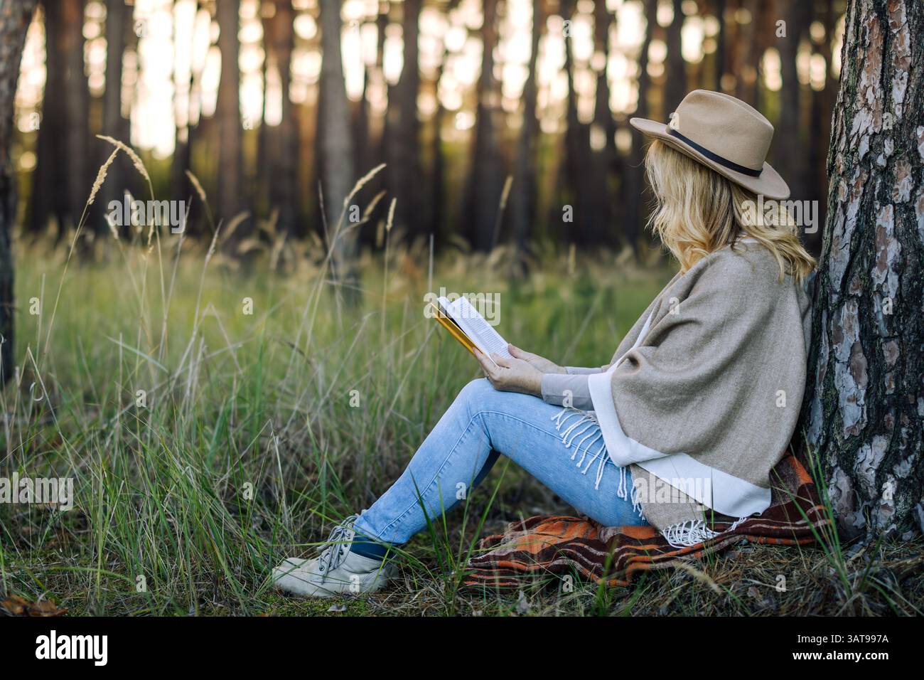 Frau, die im Wald Buch liest. Entspannung in der Natur zur Verbesserung der psychischen Gesundheit. Waldtherapie Stockfoto