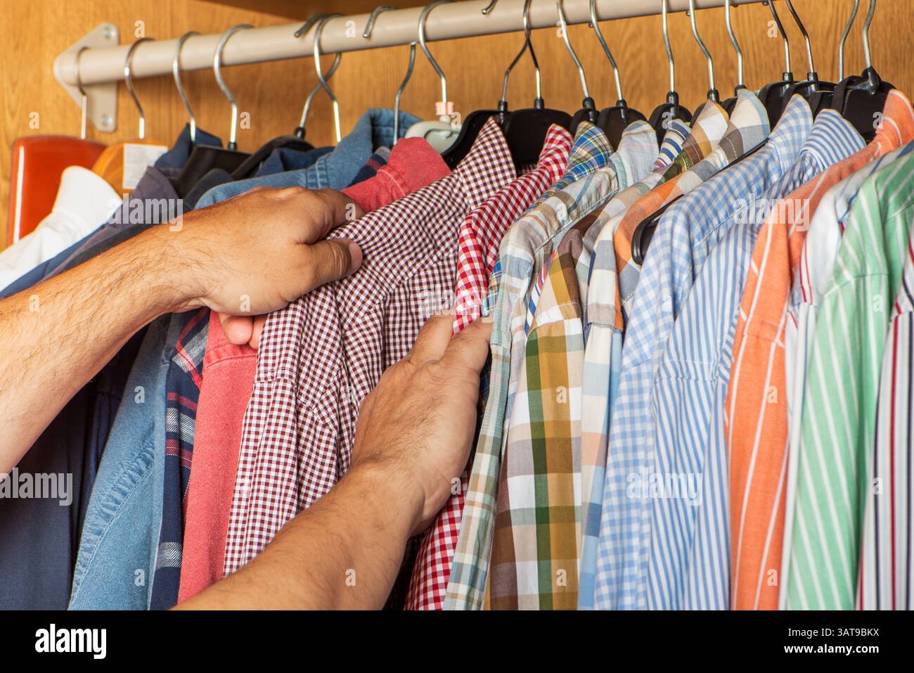 Männliche Hände wählen ein Hemd aus einer Garderobe mit einer Vielzahl von Hemden. Stockfoto
