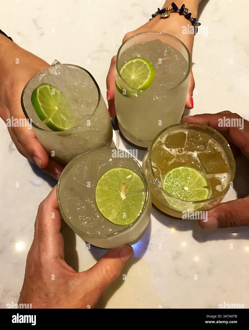 Aus nächster Nähe sehen vier Personen, die Mojito- und mai Tai-Cocktails halten und einen feierlichen Toast anstoßen Stockfoto