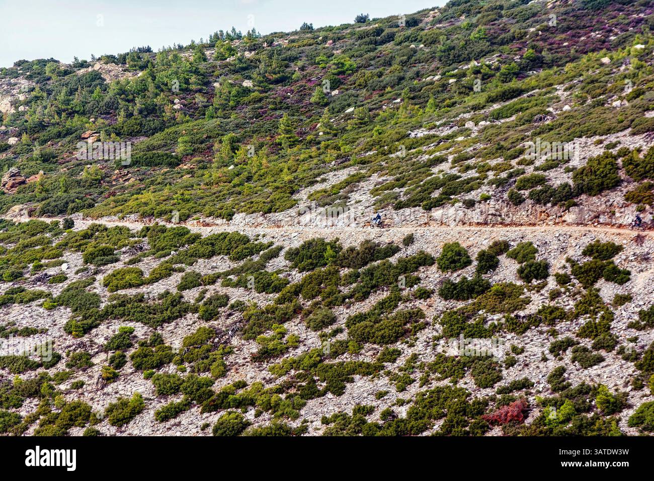 Zwei Radfahrer fahren auf einem schmalen, von Felsen und Büschen umgebenen Feldweg an einem steilen Penteli-Berg in Athen. Stockfoto