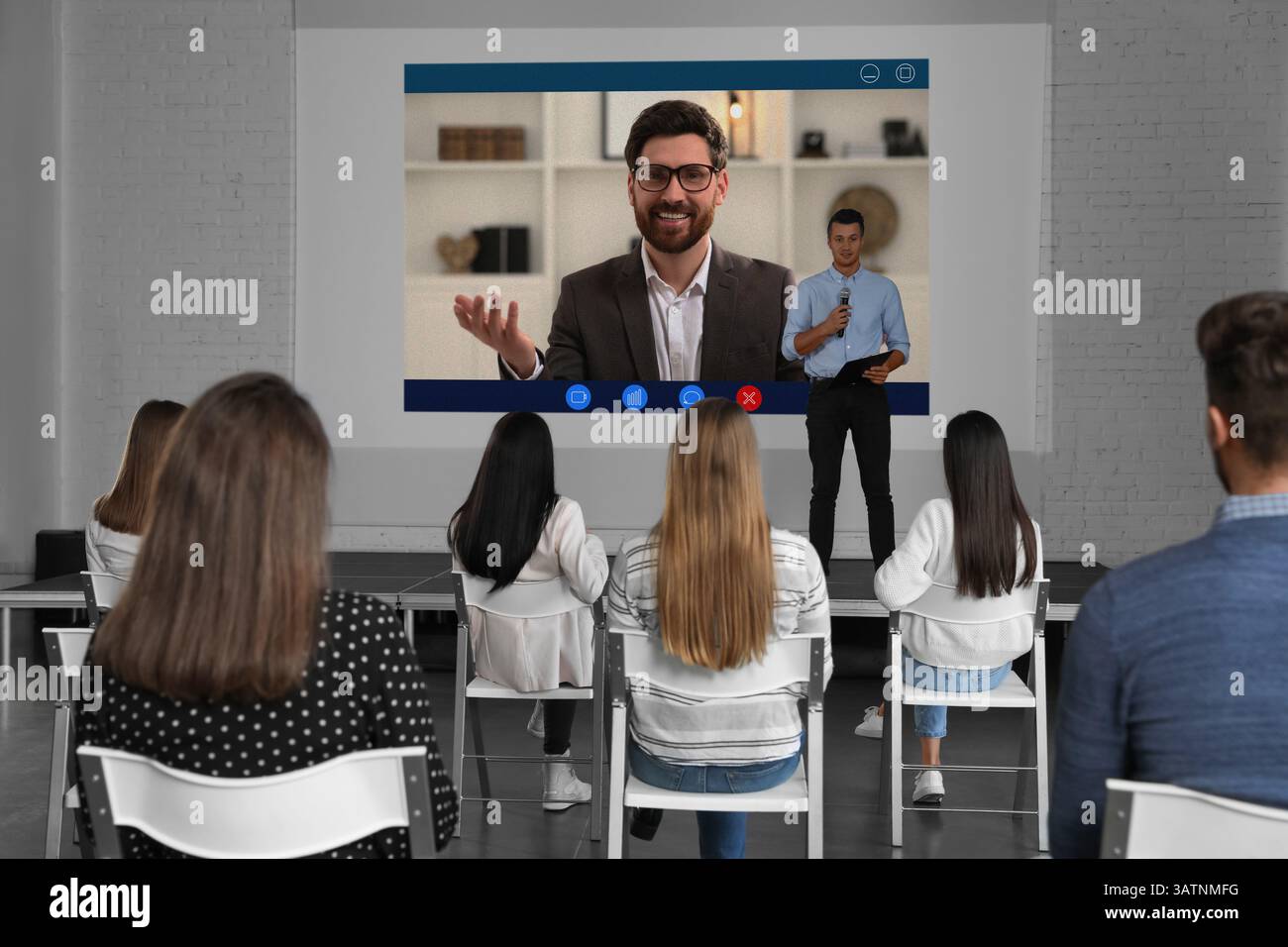 Redner, der über Online-Videochat an der Vorlesung teilnimmt. Publikum und Trainer im Konferenzraum mit Projektionsleinwand Stockfoto