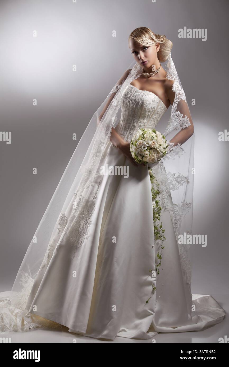 Junge schöne blonde Frau in einem Hochzeitskleid auf einem Atelierhintergrund Stockfoto