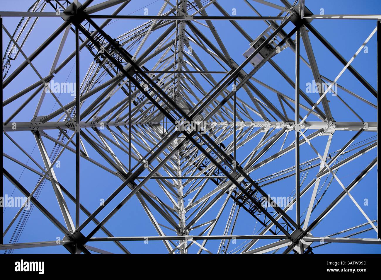 Amsterdams Blick von unten nach oben auf Stromleitungen und Metallgitter bildet einen eindrucksvollen, geometrischen Aufstieg in einen klaren blauen Himmel, der die urbane Macht wirklich verkörpert. Stockfoto