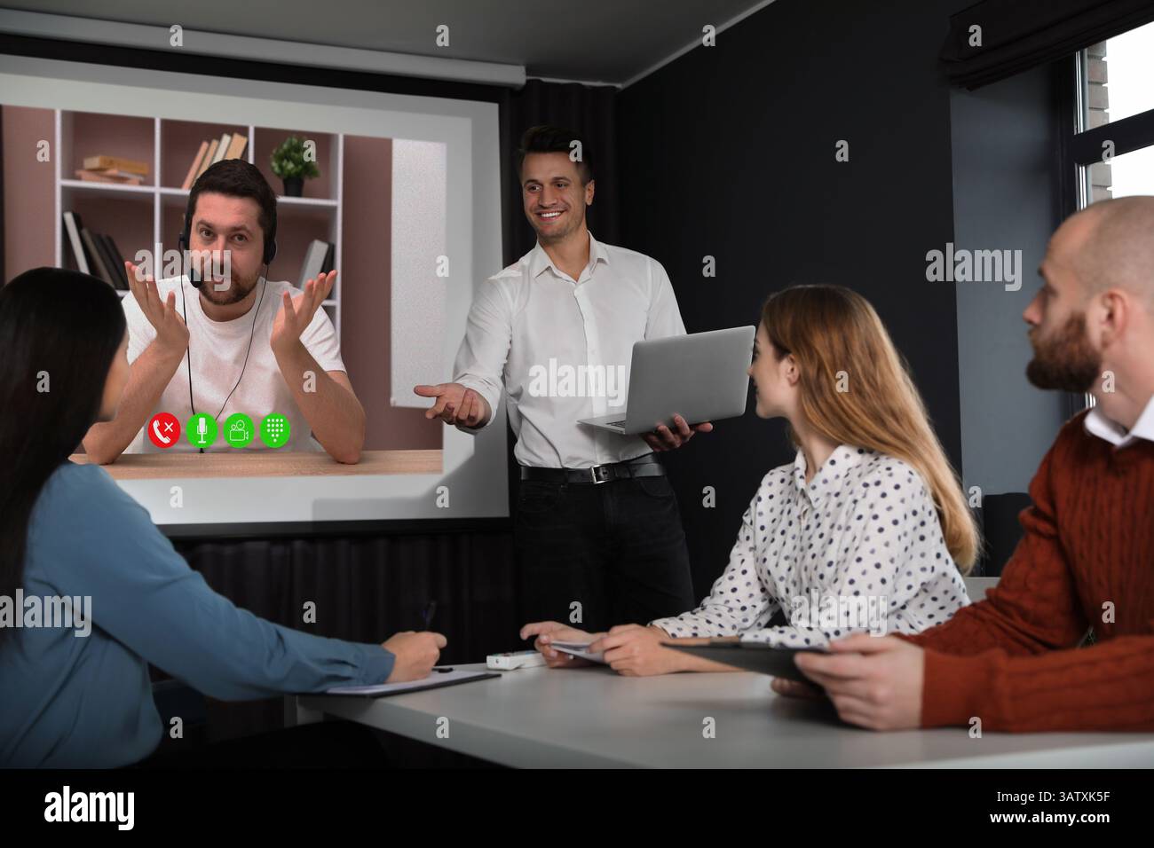 Redner, der über Online-Videochat an der Vorlesung teilnimmt. Publikum und Trainer im Konferenzraum mit Projektionsleinwand Stockfoto