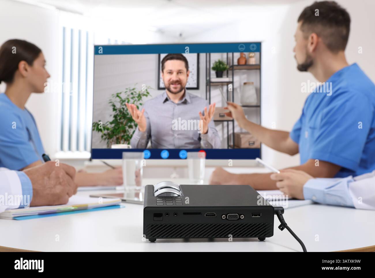Redner, der über Online-Videochat an der Vorlesung teilnimmt. Medizinisches Personal im Konferenzraum mit Projektionsleinwand Stockfoto