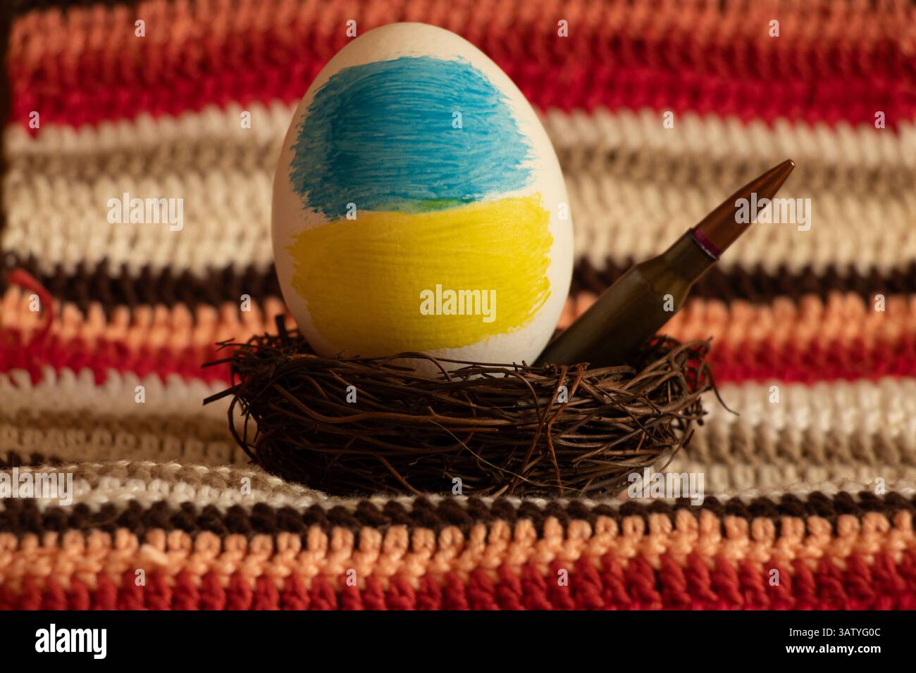 Osterei mit ukrainischer Flagge und Kugel im Nest auf gestricktem gestreiftem Hintergrund, Ostern im Krieg in der Ukraine Stockfoto