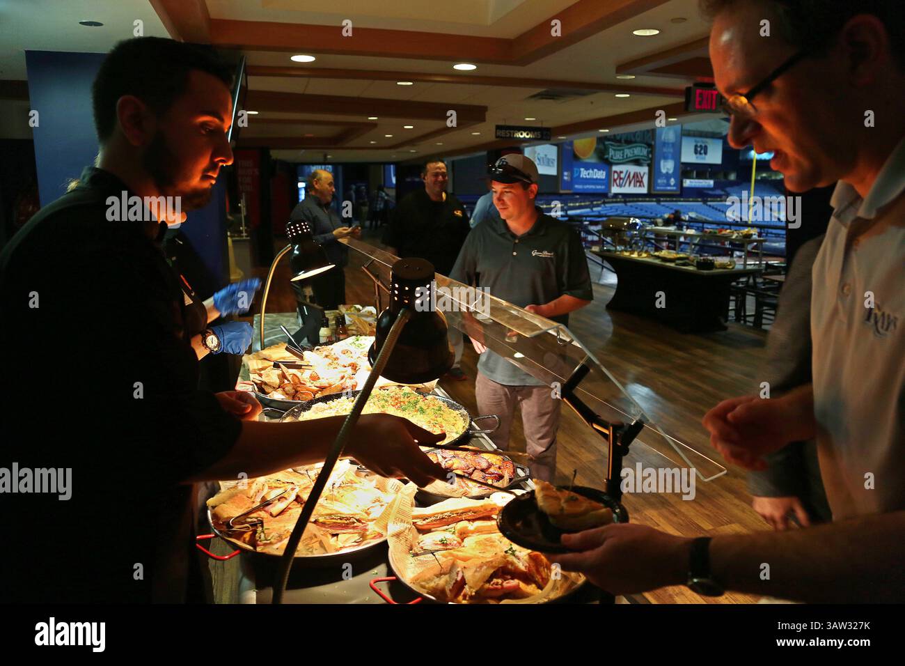 März 2016 - St. Petersburg, Florida, USA - SCOTT KEELER | Times. Pipo's Cafe Server Ramon Hernandez, St. Petersburg, links, serviert einen Teller kubanischer Speisen für Tampa Bay Rays Radiosender Andy Freed, Right, Dienstag, 3. März 29/16 im Tropicana Field. Das Zentrum ist Mason Stotz, Vertriebsleiter von Green Bench Brewing Co. Die Tampa Bay Rays und ihr Konzessionsverkäufer Centerplate haben neue gastronomische Optionen für die kommende Saison vorgestellt. Pipo's Cafe ist dieses Jahr eine Neuheit im Tropicana Field. Sie befinden sich in der Nähe von Gate 1 auf der Ebene der Feldhalle und in einem mobilen Wagen auf dem Budweiser des Stadions Stockfoto