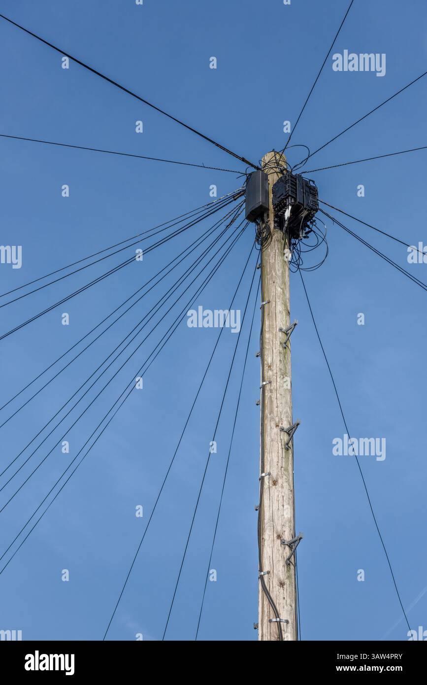 Holzmast mit moderner Telekommunikationsausrüstung und mehreren Drähten, die ein Sternmuster von der Spitze des Stabs bilden, vor einem klaren blauen Hintergrund Stockfoto