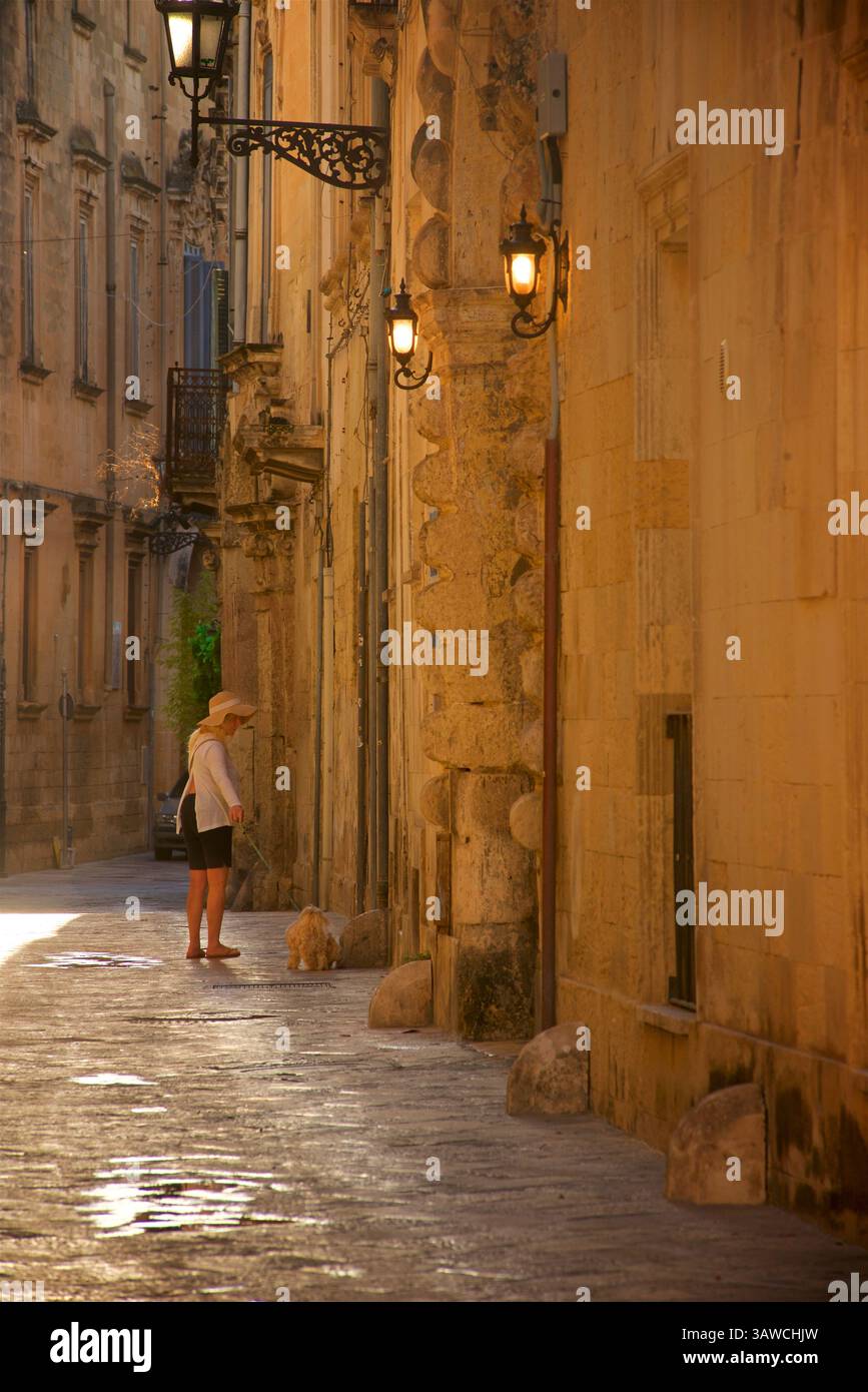Italien, Apulien, Lecce. Die Altstadt von Lecce ist ein labrynthisches gewirr aus engen Gassen und historischer Architektur. Frau, die mit einem kleinen Hund läuft. Stockfoto
