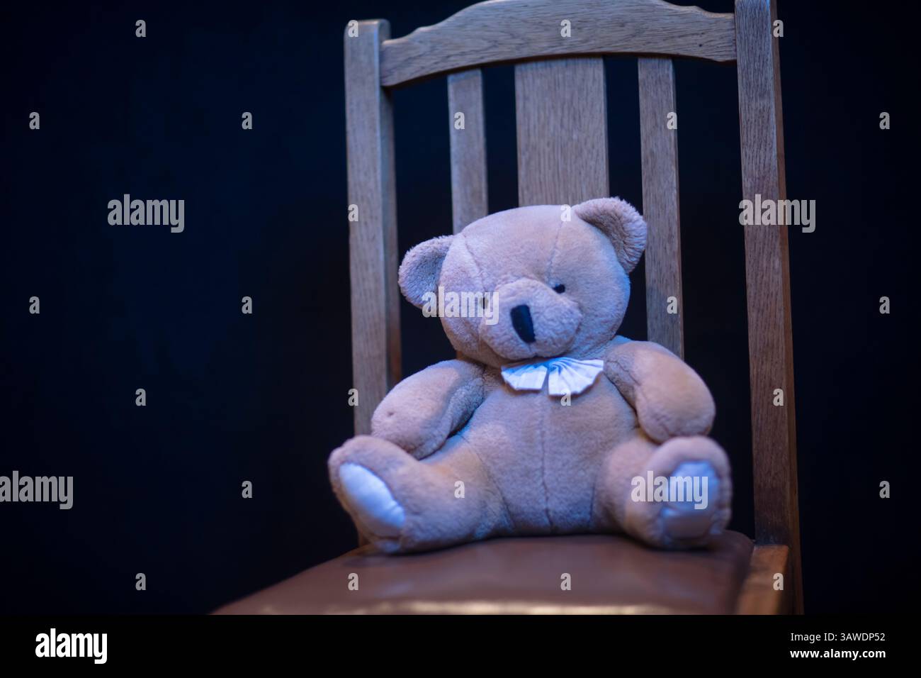 Weicher Teddybär auf einem alten Holzstuhl mit schlichtem schwarzem Hintergrund Stockfoto
