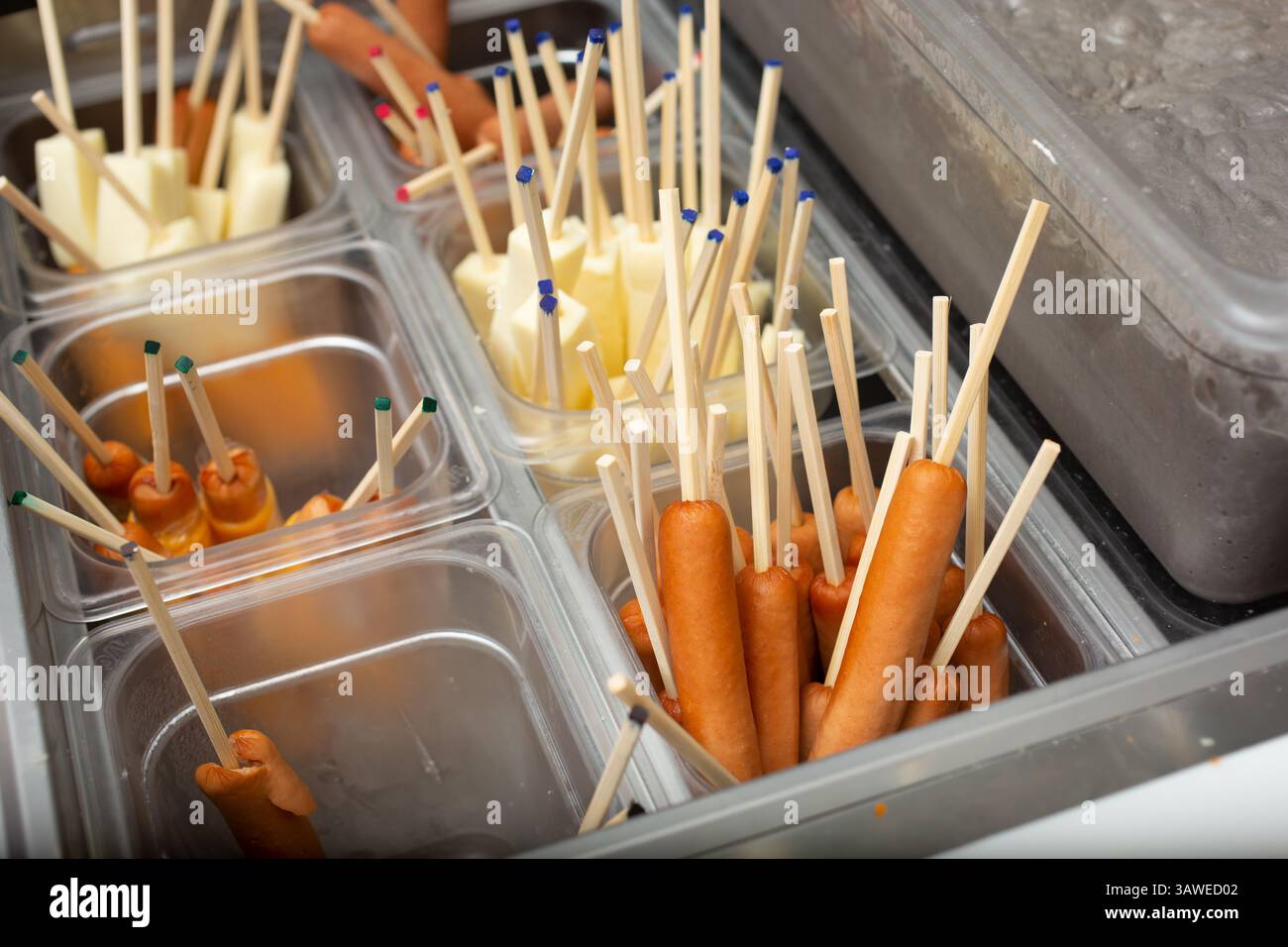 Ein Blick auf Behälter mit Hotdogs und Weißkäse auf Stöcken, gesehen in einem lokalen koreanischen Reis Hot Dog Restaurant. Stockfoto
