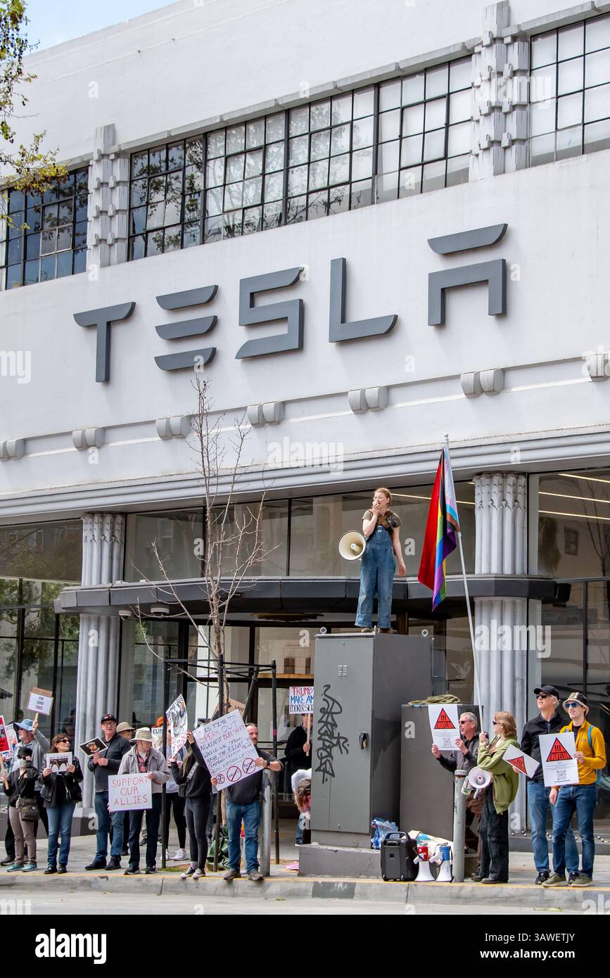 San Francisco, USA. April 2025. Die Demonstranten versammeln sich vor dem Tesla-Ausstellungsraum und -Händlerbetrieb in San Francisco, während eine junge Frau unter ihnen auf einem Versorgungskasten mit Megaphon direkt unter dem TESLA-Schild auf dem Gebäude steht. Quelle: Shelly Rivoli/Alamy Live News Stockfoto