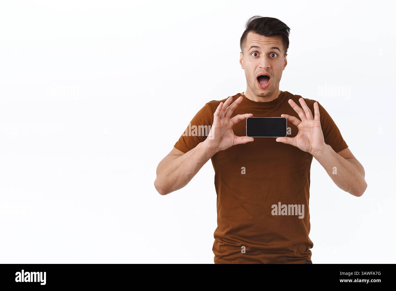 Wow cool, sieh es aus. Überrascht und gewundert, ein gutaussehender Erwachsener im braunen T-Shirt reagiert auf neues Video wurde viral auf Smartphone-App und zeigt mobile Pho Stockfoto