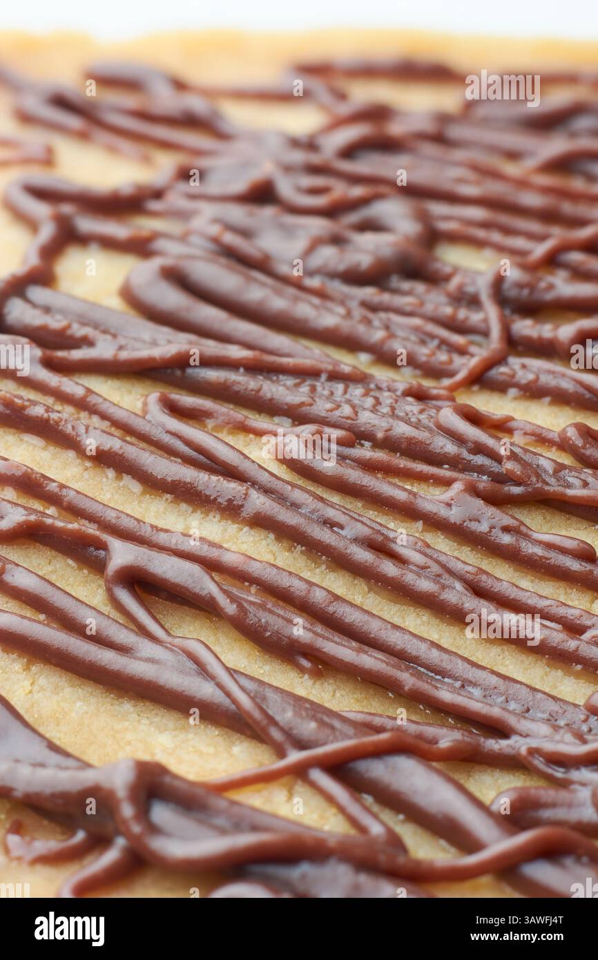 Nahaufnahme von dunkelbraunem Schokoladenbelag auf der Kuchenoberfläche, überkreuzte dicke, unregelmäßige, wellige Musterlinien, weicher Fokus mit unscharfem Hintergrund Stockfoto